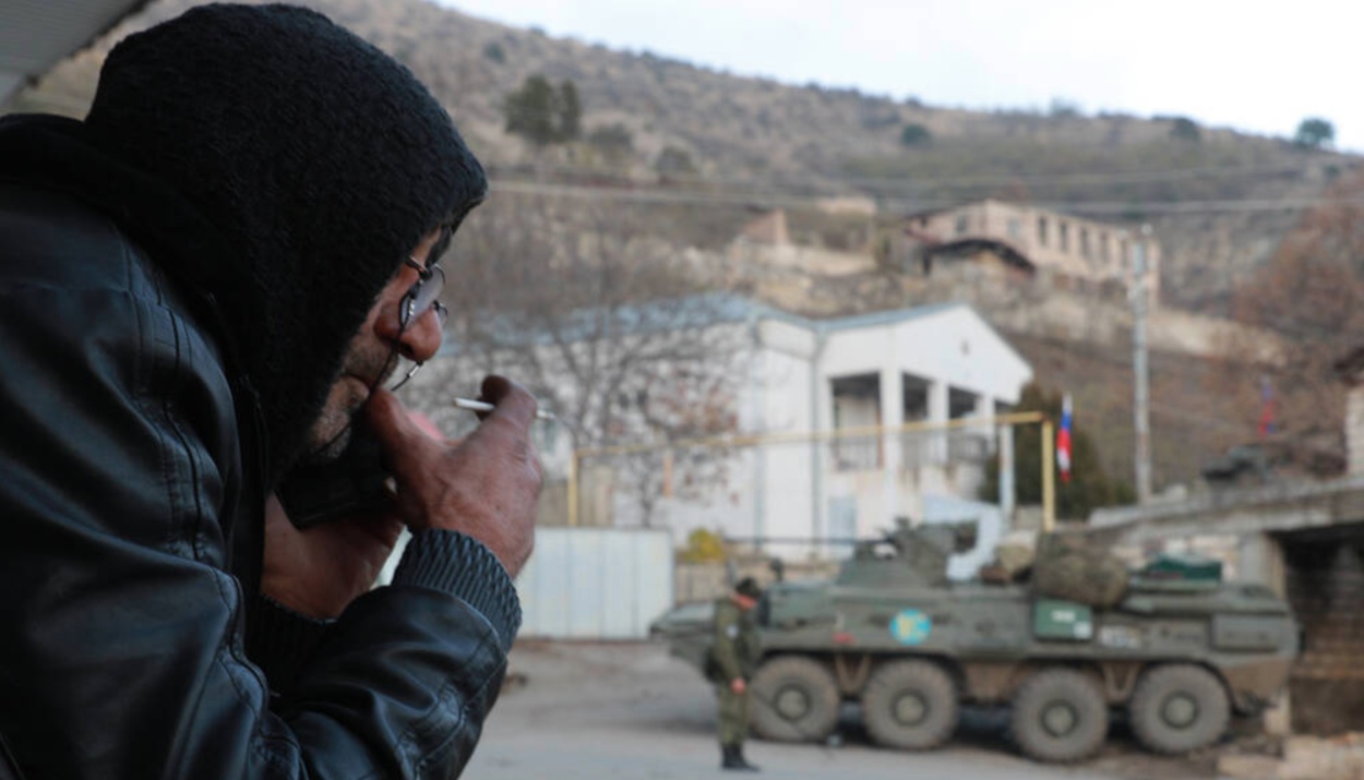 A local man smoking against the background of Russian peackeepers in the town of Lachin (Berdzor).